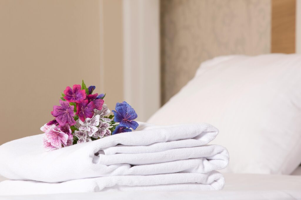 Cozy hotel room featuring stacked white towels and vibrant flowers for a welcoming touch.